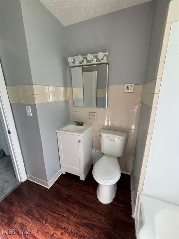 bathroom with vanity, wood finished floors, a textured ceiling, tile walls, and toilet