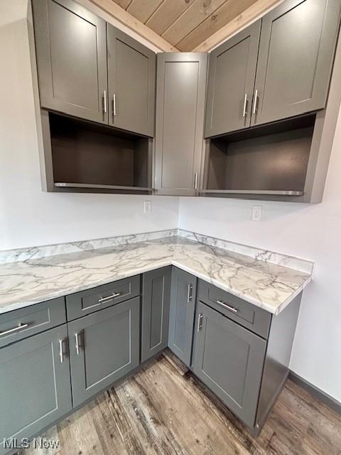 kitchen featuring light wood finished floors, gray cabinetry, light stone counters, wooden ceiling, and open shelves