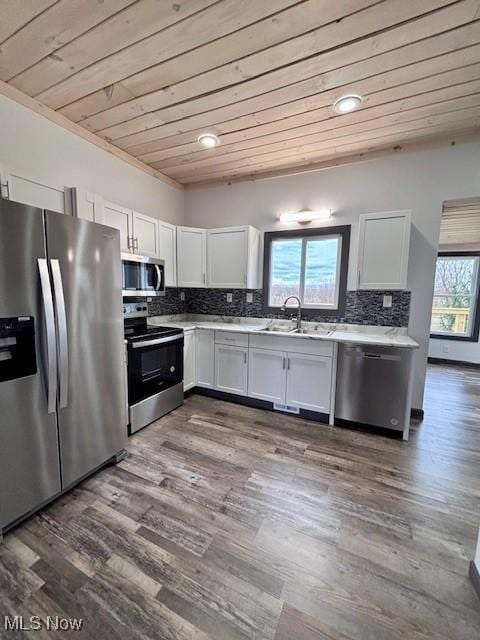 kitchen with a sink, light countertops, appliances with stainless steel finishes, wooden ceiling, and tasteful backsplash