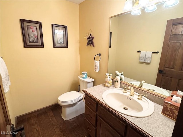 half bath featuring vanity, baseboards, toilet, and wood finished floors