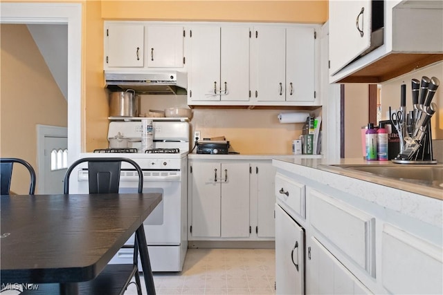 kitchen with light floors, white range with gas cooktop, light countertops, under cabinet range hood, and white cabinetry