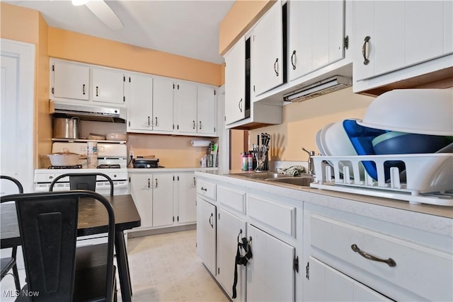 kitchen featuring white gas stove, under cabinet range hood, white cabinets, light countertops, and light floors