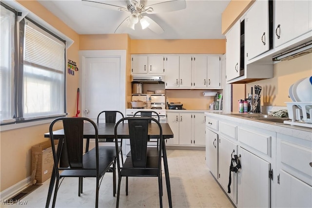 kitchen featuring baseboards, ceiling fan, under cabinet range hood, light countertops, and white cabinetry