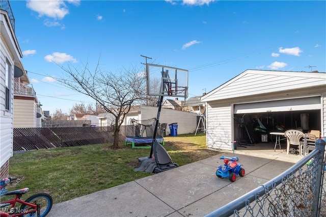 view of yard with fence, an outdoor structure, a garage, a trampoline, and a patio area