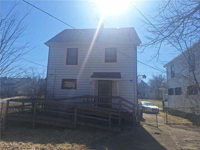 view of front of home with a deck, fence, and a shingled roof