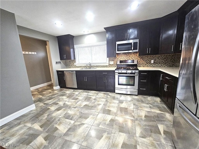 kitchen with baseboards, a sink, light countertops, appliances with stainless steel finishes, and backsplash