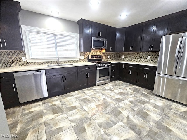 kitchen featuring a sink, backsplash, stainless steel appliances, light countertops, and dark cabinets