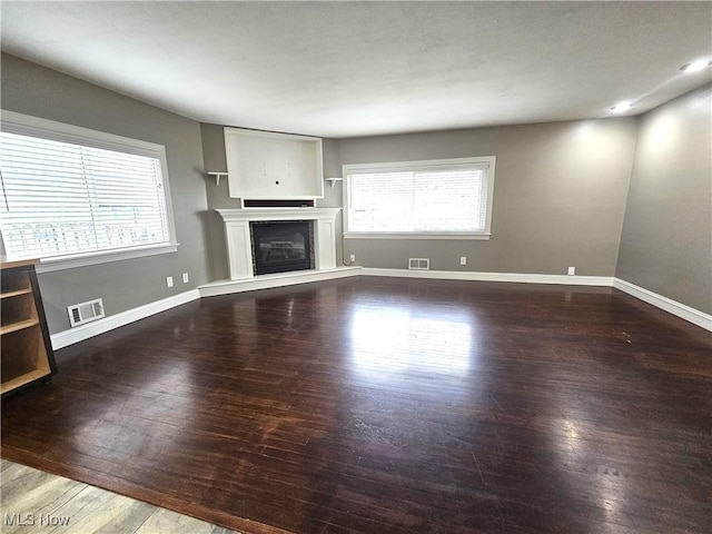 unfurnished living room featuring a glass covered fireplace, wood finished floors, visible vents, and baseboards