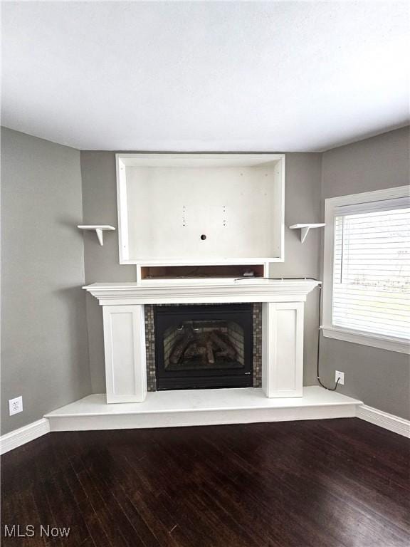 unfurnished living room with a glass covered fireplace, baseboards, and wood finished floors