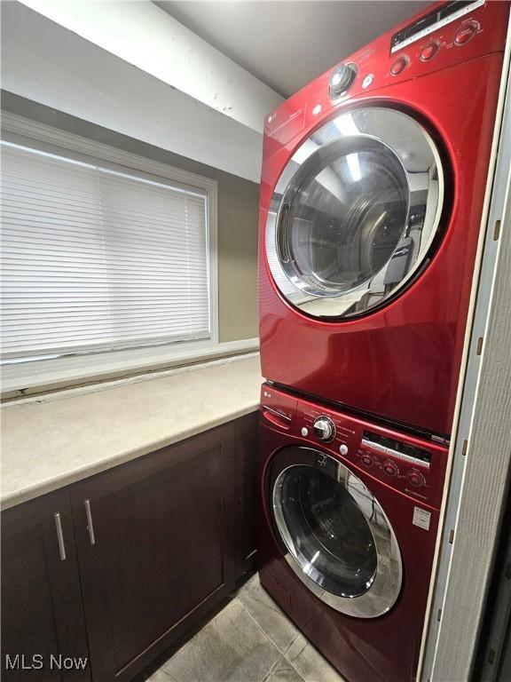 laundry area featuring light tile patterned floors, cabinet space, and stacked washer and clothes dryer