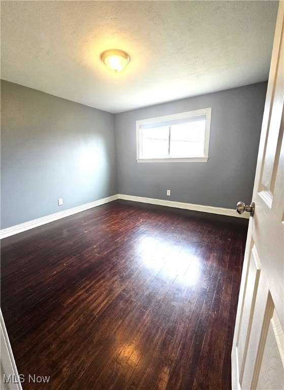 spare room with baseboards, a textured ceiling, and dark wood-style flooring