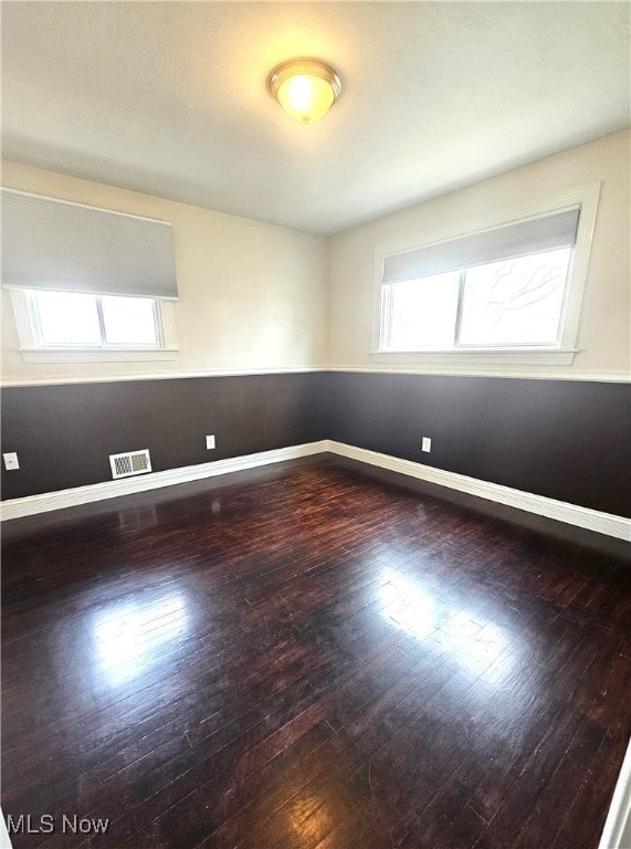 empty room with visible vents, baseboards, and hardwood / wood-style flooring