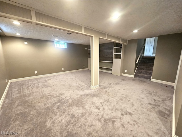 basement with stairs, carpet flooring, baseboards, and a textured ceiling