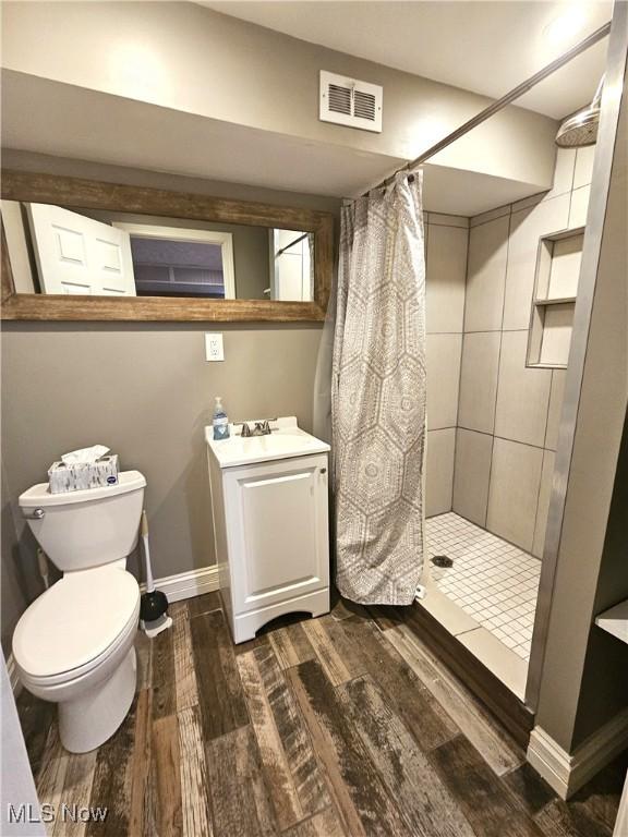 bathroom with visible vents, toilet, wood finished floors, baseboards, and tiled shower