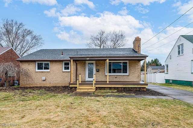 view of front of house with brick siding, fence, a porch, a front yard, and a chimney