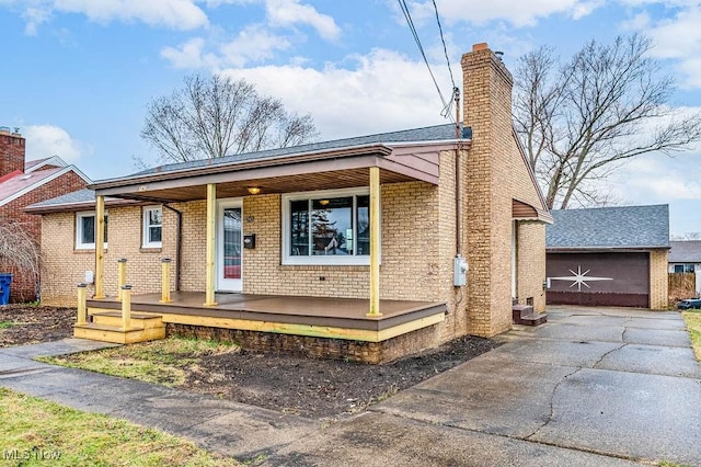 view of front of house with covered porch, a chimney, an outdoor structure, a garage, and brick siding