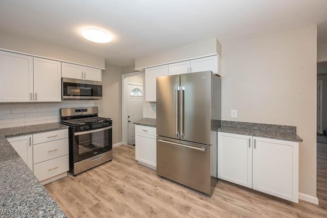 kitchen with light wood finished floors, dark stone counters, stainless steel appliances, white cabinetry, and backsplash