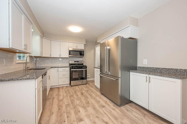 kitchen featuring dark stone countertops, a sink, decorative backsplash, appliances with stainless steel finishes, and white cabinetry