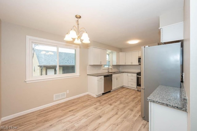 kitchen featuring baseboards, light wood finished floors, visible vents, decorative backsplash, and appliances with stainless steel finishes