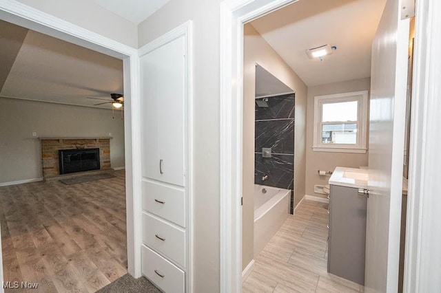 full bath with vanity, wood finished floors, a ceiling fan, baseboards, and a fireplace