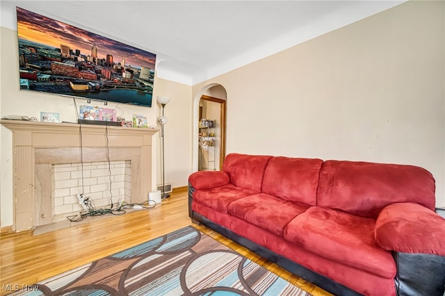 living room with arched walkways, a fireplace with flush hearth, visible vents, and wood finished floors