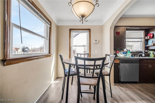 dining area featuring light wood-style flooring, baseboards, and arched walkways