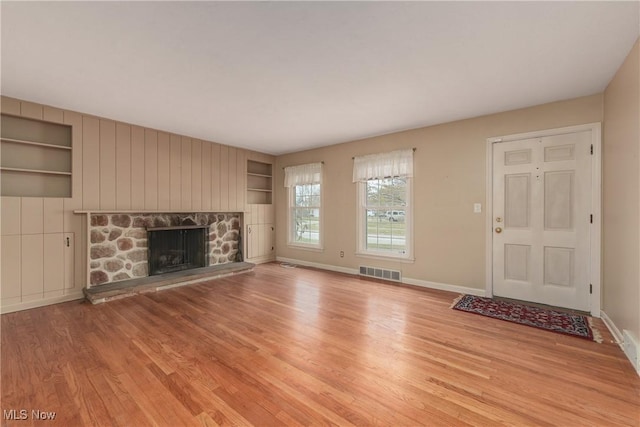 unfurnished living room with visible vents, built in features, wood finished floors, a fireplace, and baseboards