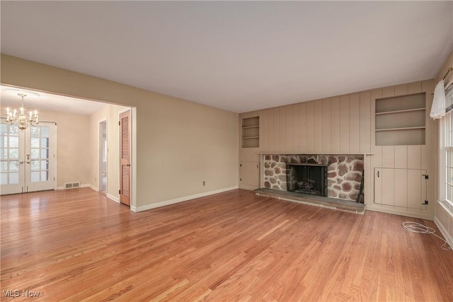 unfurnished living room featuring visible vents, built in shelves, baseboards, light wood-style floors, and an inviting chandelier