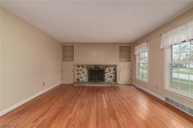 unfurnished living room with built in features, visible vents, baseboards, and light wood-style floors