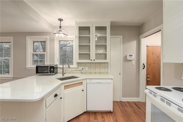 kitchen with light countertops, decorative backsplash, light wood-style floors, white appliances, and a sink