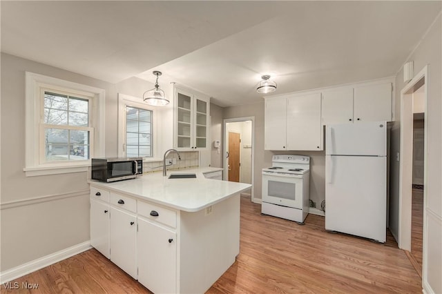 kitchen with a sink, white appliances, light wood-style floors, a peninsula, and glass insert cabinets