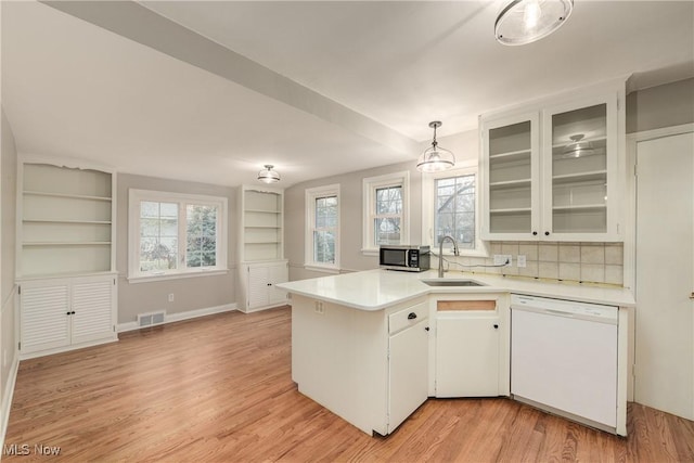 kitchen with visible vents, a peninsula, white dishwasher, a sink, and light countertops