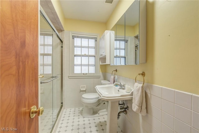 bathroom featuring a wainscoted wall, toilet, a stall shower, tile walls, and a sink