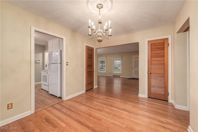 unfurnished dining area with light wood-type flooring, baseboards, an inviting chandelier, and visible vents