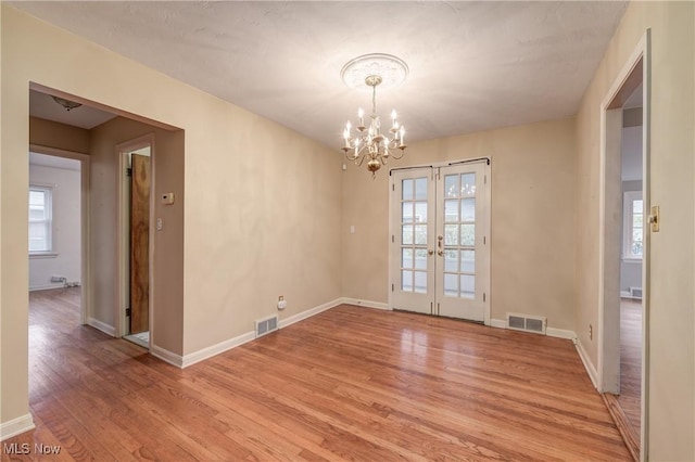 unfurnished dining area with visible vents, light wood-style floors, a chandelier, and french doors