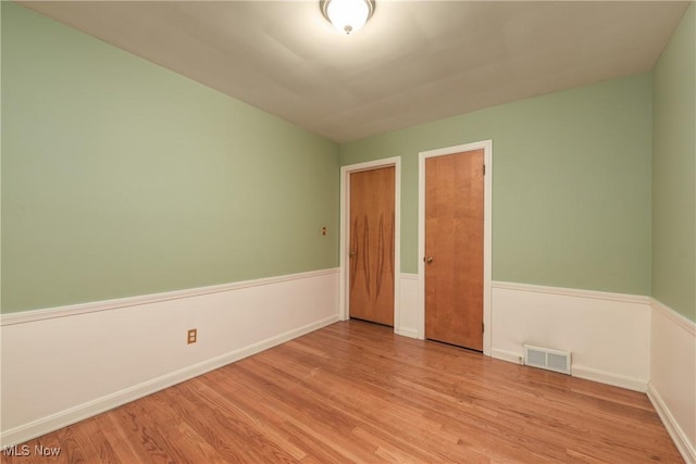 spare room with a wainscoted wall, visible vents, and light wood finished floors