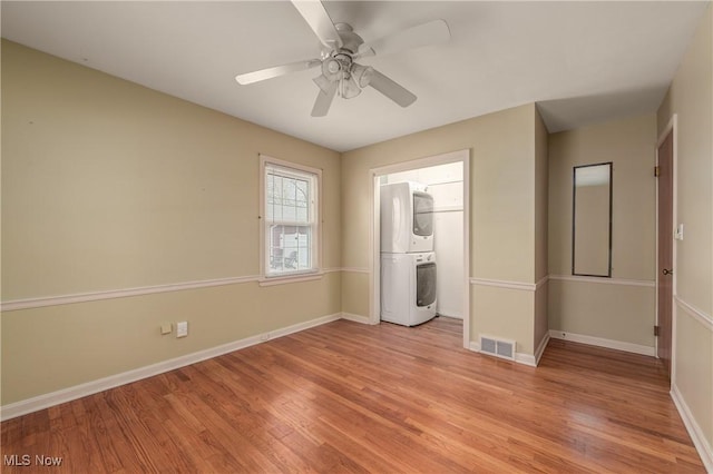 unfurnished bedroom featuring light wood finished floors, visible vents, baseboards, stacked washer and clothes dryer, and a ceiling fan