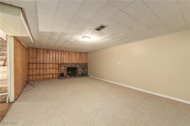 unfurnished living room with visible vents, baseboards, a fireplace, wood walls, and light colored carpet