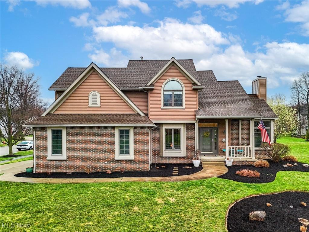 view of front facade with a chimney, a front yard, brick siding, and roof with shingles