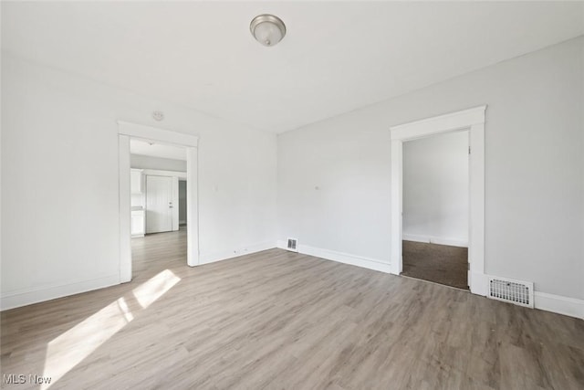 spare room with wood finished floors, visible vents, and baseboards