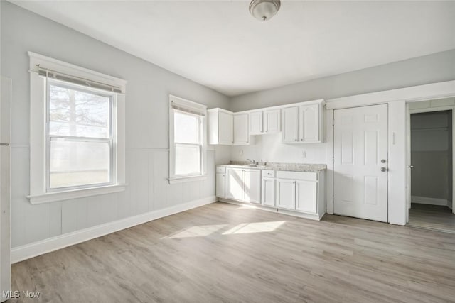 kitchen featuring light wood-style flooring, white cabinetry, wainscoting, light countertops, and baseboards