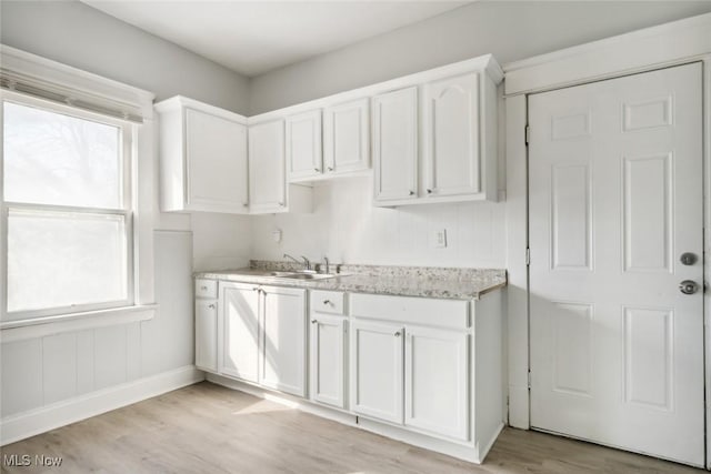 kitchen with light wood-type flooring, a sink, light stone counters, white cabinets, and baseboards