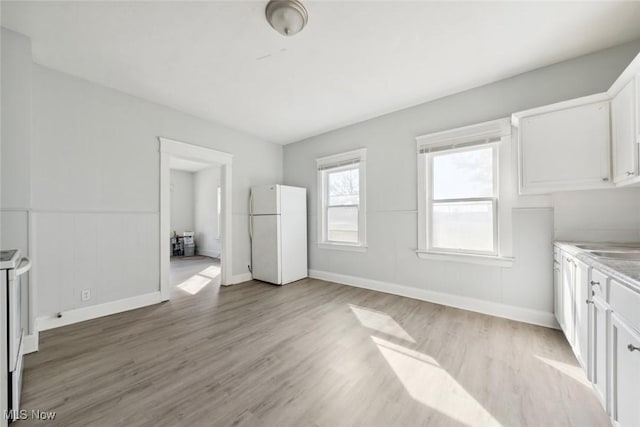 unfurnished bedroom with light wood finished floors, a wainscoted wall, freestanding refrigerator, and baseboards