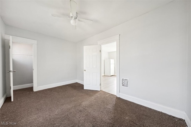 unfurnished bedroom with visible vents, dark carpet, freestanding refrigerator, and baseboards