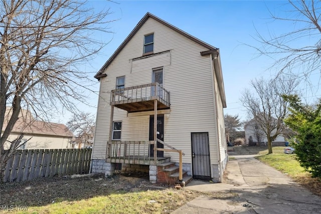 rear view of house featuring a balcony and fence