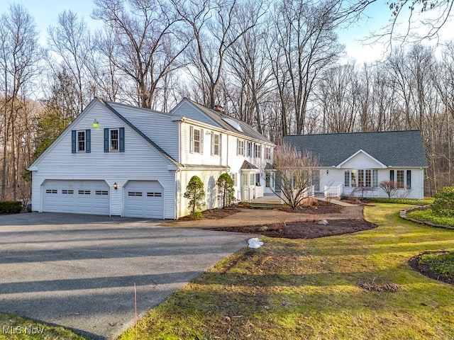 view of front facade with a garage, a front yard, a chimney, and aphalt driveway