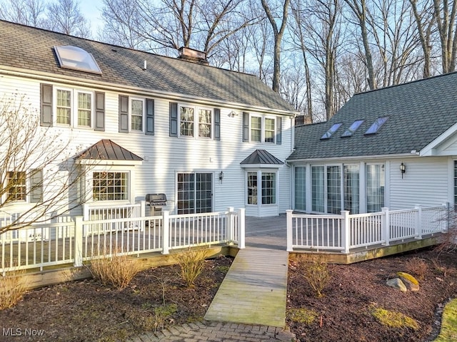 view of front facade with a deck, a standing seam roof, and a chimney