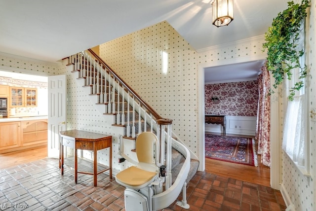 staircase with baseboards, wallpapered walls, crown molding, and brick floor