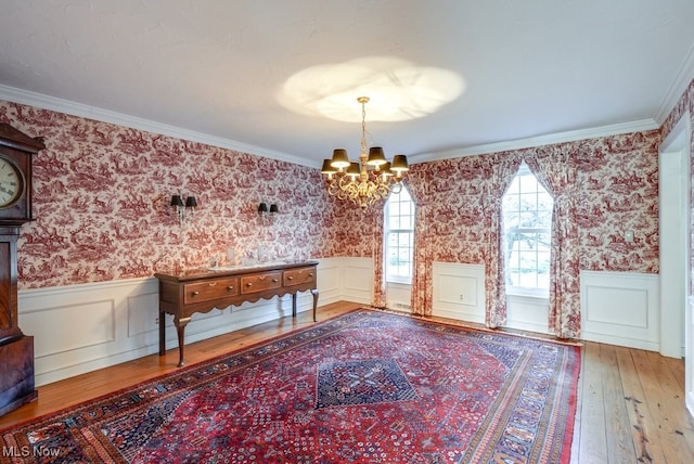 unfurnished dining area featuring a chandelier, a wainscoted wall, wallpapered walls, and ornamental molding