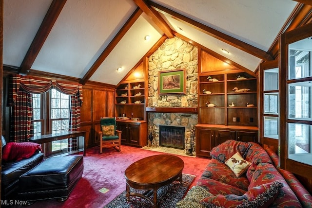 carpeted living room featuring a stone fireplace, lofted ceiling with beams, and built in shelves